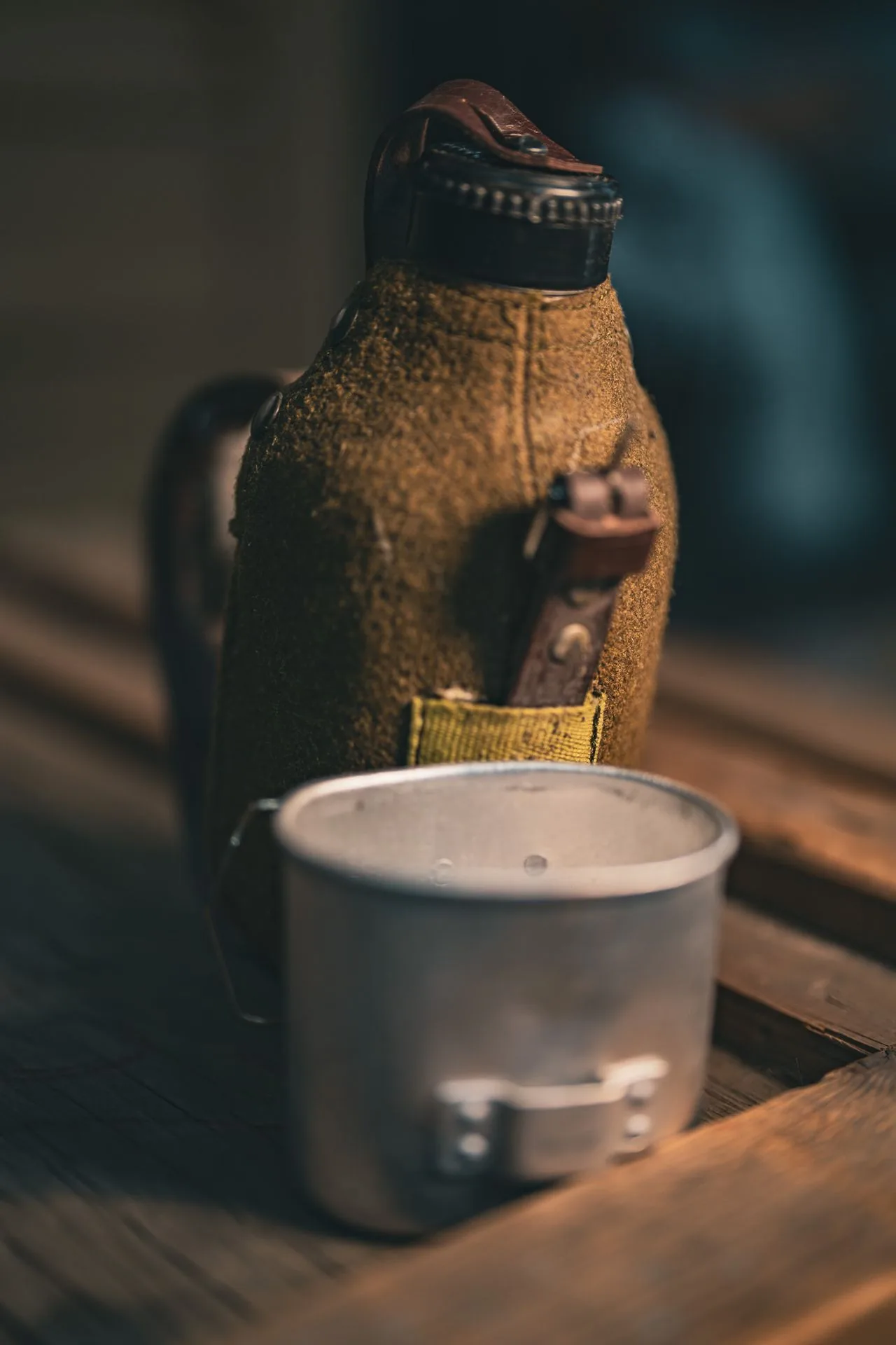 Romanian canteen with wool cover in the background and the aluminum drinking cup separated in the foreground, on a wood plank