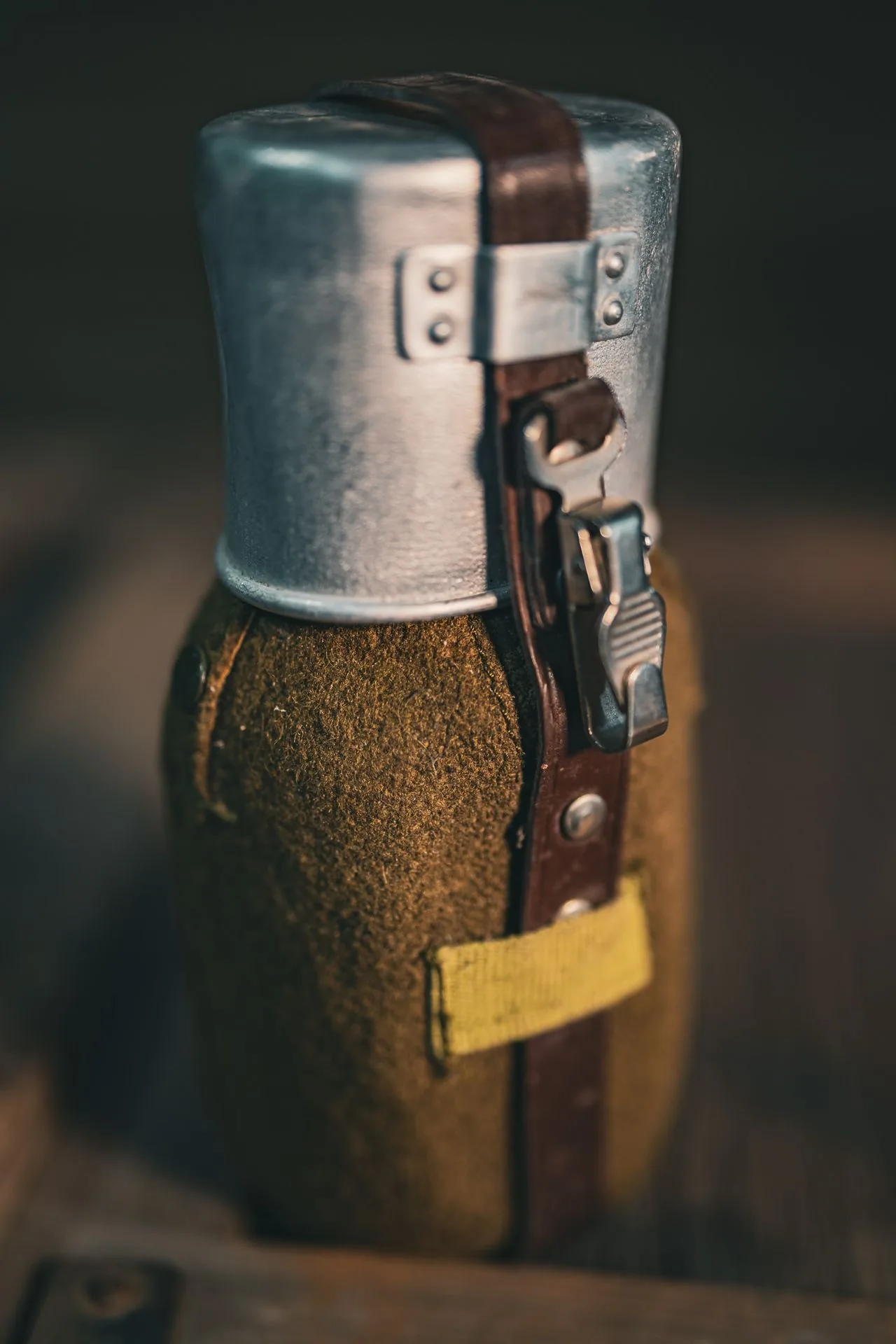 Side profile of the Romanian canteen with the cup nested on top and the leather strap running over both, showing wear that is typical of issued surplus