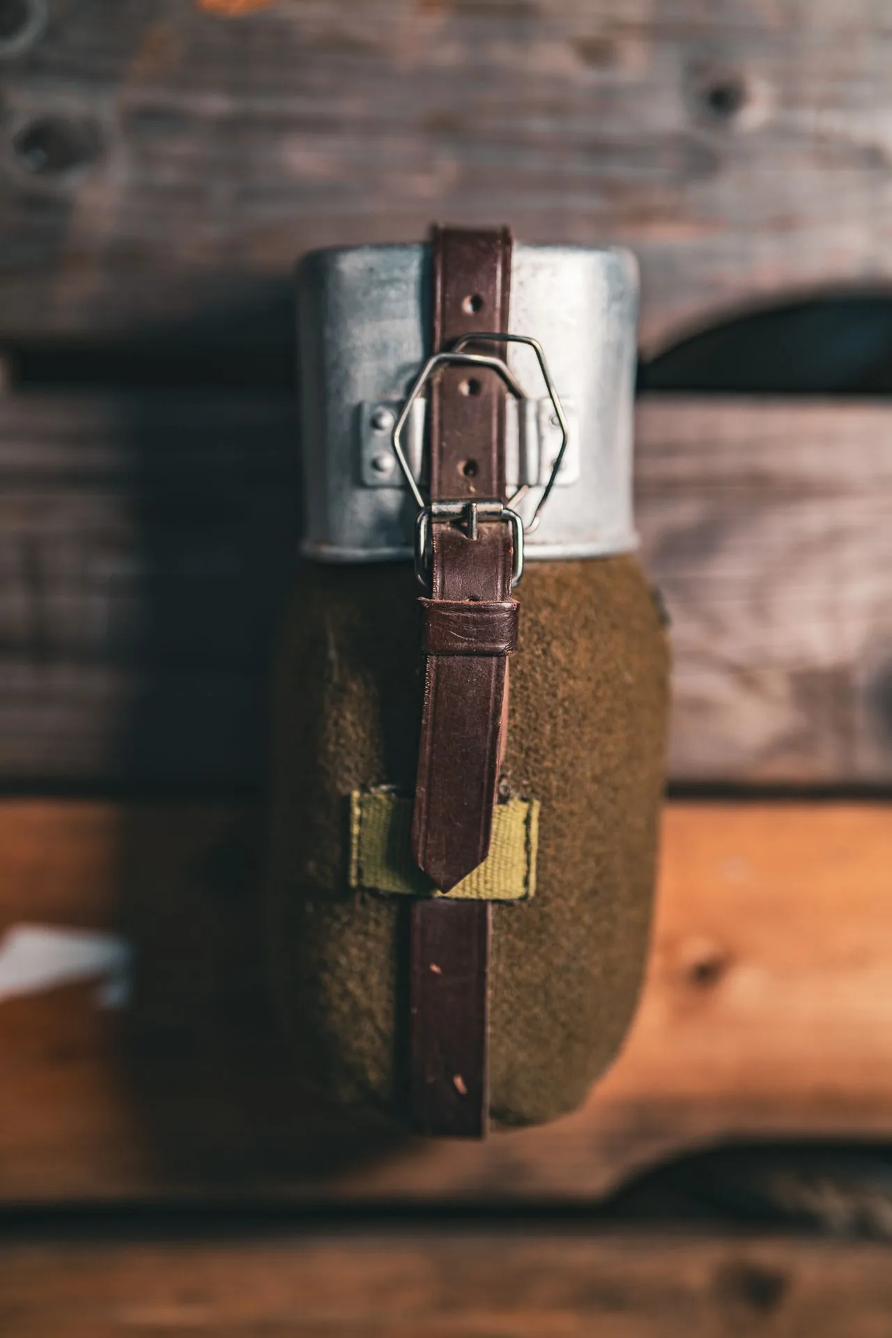 Long leather retaining strap running down the length of the wool-covered Romanian canteen, buckling into a woven olive belt loop