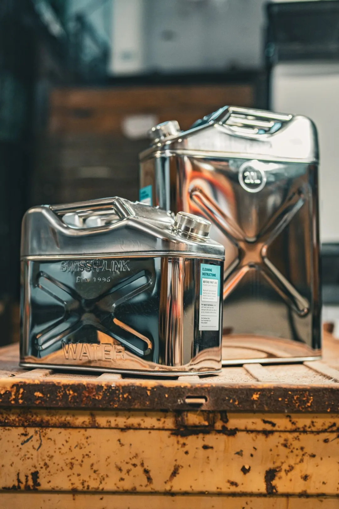 Swiss Link stainless steel water cans in 10 liter and 20 liter sizes shown together on a storage crate, with SWISS-LINK WATER embossed panel visible